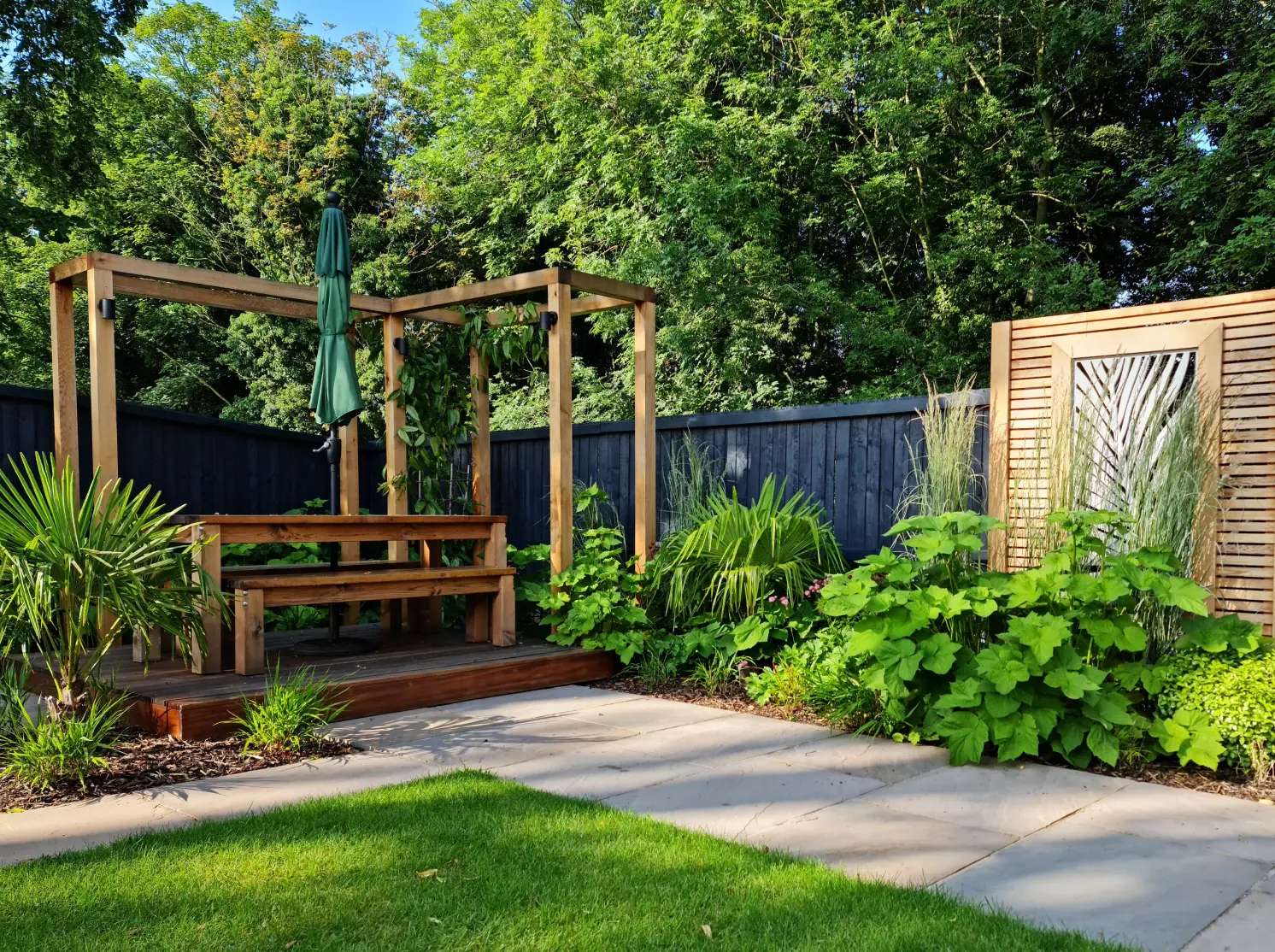Finished courtyard garden in Malpas with timber pergola, lush planting and sandstone paving