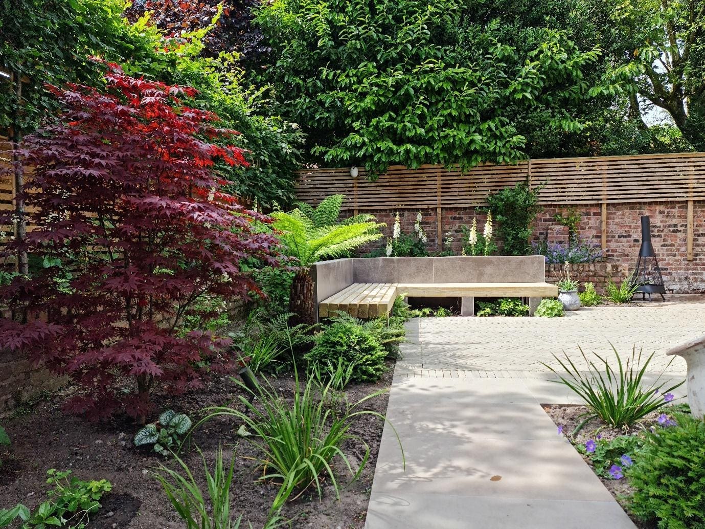 Soft natural garden in Altrincham with porcelain paving, lush planting and built-in bench seating