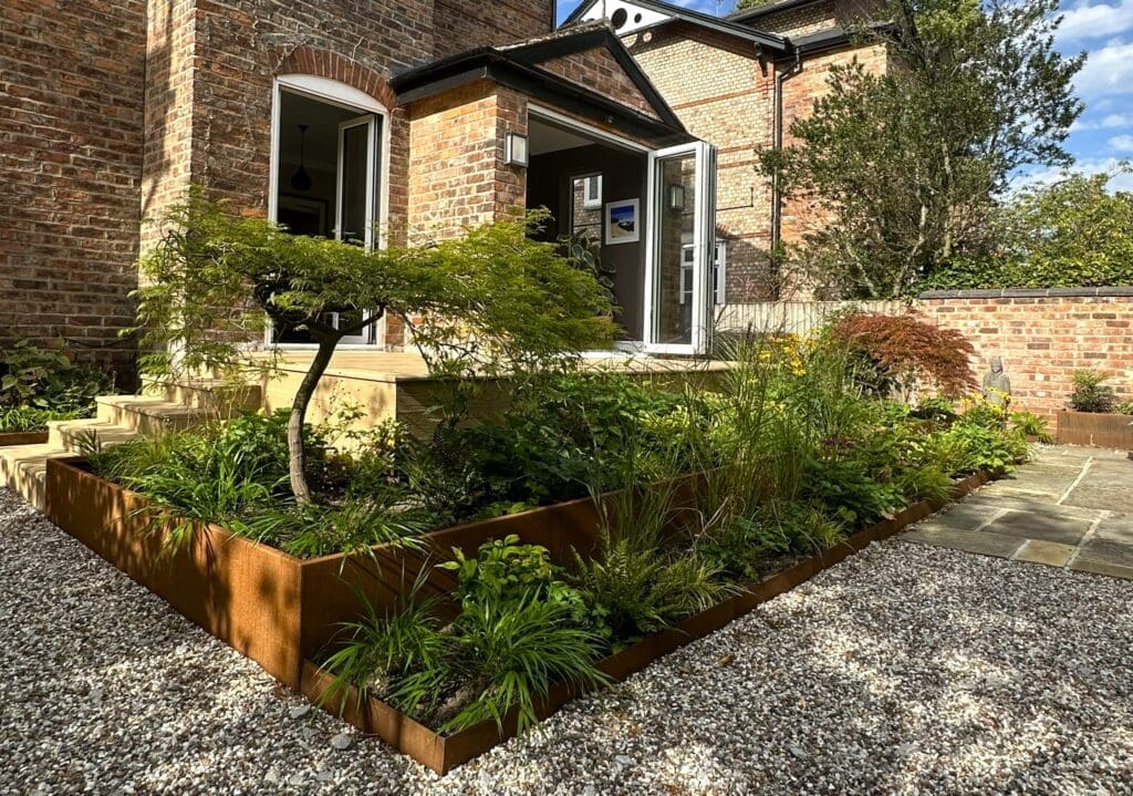 A modern garden design featuring a mix of plants and a decorative tree near a brick house.